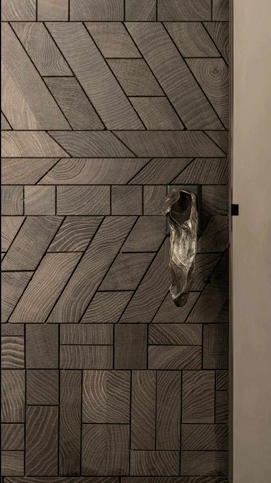 A door faced in Forêt endgrain oak, its patterns changing band by band, with a cast bronze handle